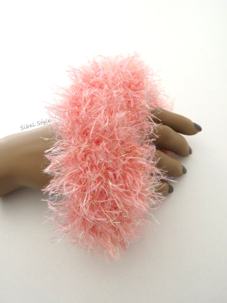 Puede incluir: Un coletero de color rosa claro, esponjoso y hecho de hilo texturizado y desgre&ntilde;ado con sutiles fibras iridiscentes entrelazadas. El accesorio presenta un aspecto suave y voluminoso e incluye el texto Sibel Style impreso en negro a la izquierda.