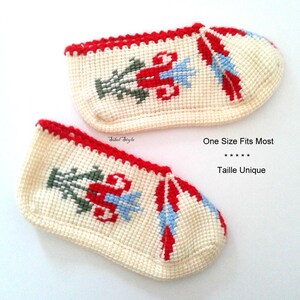 May include: A pair of off-white crochet slippers featuring a red, light blue, and dark green floral pattern. The slippers have a red trim along the top edge and include the text Sibel Style and One Size Fits Most printed on the image.
