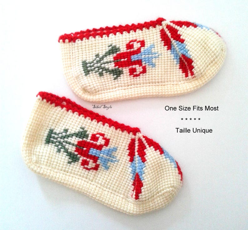 May include: A pair of off-white crochet slippers featuring a red, light blue, and dark green floral pattern. The slippers have a red trim along the top edge and include the text Sibel Style and One Size Fits Most printed on the image.