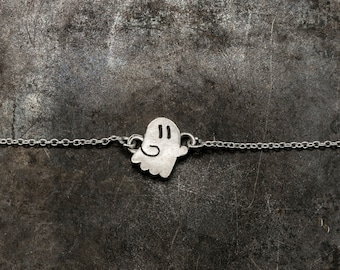 Può includere: Una collana a catena d'argento con un ciondolo a forma di fantasma. Il fantasma ha due occhi e un piccolo sorriso.
