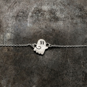 Op de afbeelding: Een zilveren ketting met een spookbedel. Het spook heeft twee ogen en een kleine glimlach.