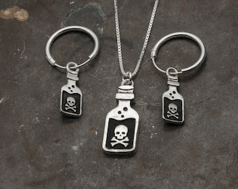 May include: Three silver charm necklaces with a skull and crossbones bottle charm. The charms are attached to a silver chain and a silver hoop.