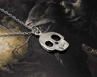 May include: A silver skull pendant necklace with a chain. The pendant is a cutout design with a detailed skull shape.