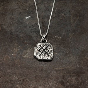 May include: Silver necklace with a textured pendant featuring a Norse symbol. The pendant is a square shape with rounded edges.