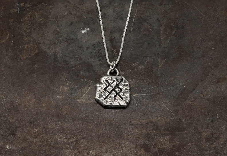 May include: Silver necklace with a textured pendant featuring a Norse symbol. The pendant is a square shape with rounded edges.
