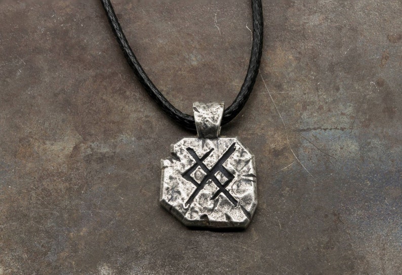 May include: A silver pendant necklace with a black leather cord. The pendant is a textured, octagonal shape with a symbol etched into it.