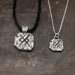 May include: Two silver necklaces with a square pendant featuring a stylized symbol. The pendant on the longer necklace is larger than the pendant on the shorter necklace.