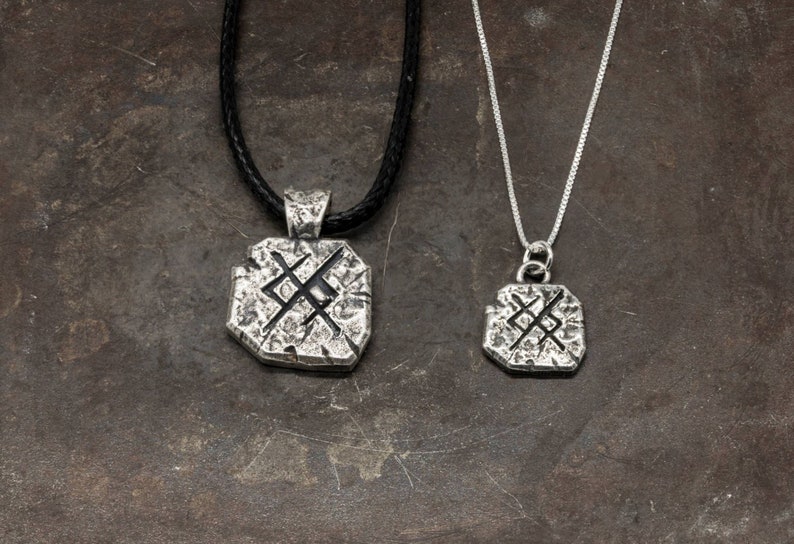 May include: Two silver necklaces with a square pendant featuring a stylized symbol. The pendant on the longer necklace is larger than the pendant on the shorter necklace.