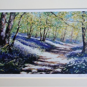 Könnte beinhalten: Ein Aquarellbild eines Weges durch einen Wald mit blühenden Blausternen. Der Weg ist von Bäumen gesäumt und das Sonnenlicht scheint durch die Blätter. Das Bild trägt den Titel "The Secret Bluebell Path" und ist vom Künstler "Adam & Garden" signiert.
