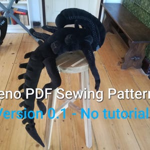 May include: A black plush Xenomorph creature, a sewing pattern design, rests on a wooden stool. The creature has a long, segmented tail and a detailed head. The text "Xeno PDF Sewing Pattern" and "Version 0.1 - No tutorial" are visible.