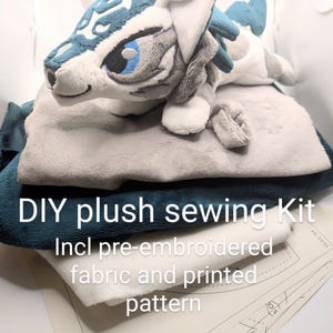May include: A DIY plush sewing kit featuring a plush toy with blue and white accents. The kit includes pre-embroidered fabric and a printed pattern. The plush toy has a detailed design with blue eyes and a gray mane.