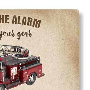 May include: A vintage-style red and black fire truck model with a ladder, set against a tan background. The text "THE ALARM your gear" is printed in brown. The model has detailed features like wheels and a ladder.