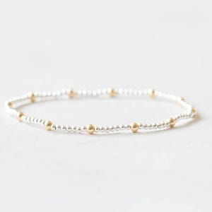 May include: A delicate bracelet featuring small silver beads interspersed with gold-colored beads. The bracelet is strung on a flexible band, creating a simple yet elegant design. This piece of jewelry is suitable for everyday wear.