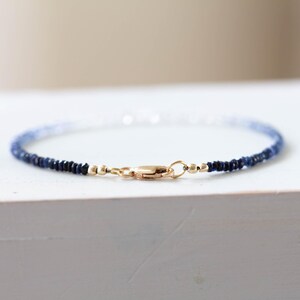 May include: Delicate bracelet featuring small, dark blue beads that fade to lighter blue and white. The bracelet is secured with a gold-colored clasp. This piece of jewelry is perfect for everyday wear.