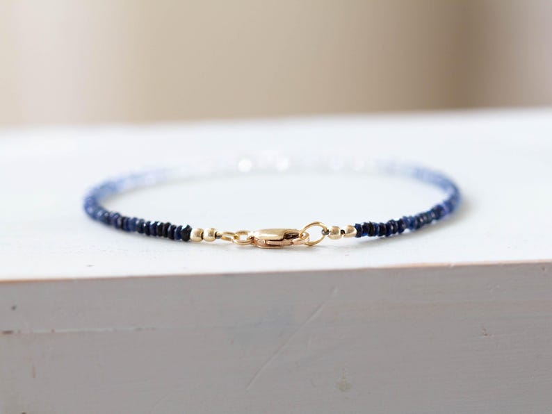 May include: Delicate bracelet featuring small, dark blue beads that fade to lighter blue and white. The bracelet is secured with a gold-colored clasp. This piece of jewelry is perfect for everyday wear.