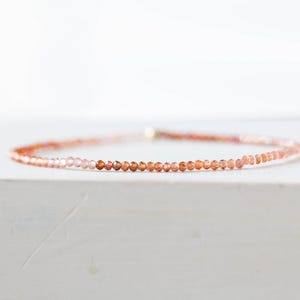 May include: Delicate bracelet featuring small, round, orange-toned beads. The beads are strung together, creating a subtle, elegant accessory. The bracelet is set against a white background, highlighting its color and design.
