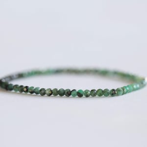 May include: A delicate bracelet featuring small, faceted emerald beads. The beads are a deep green color, strung together to form a simple, elegant accessory. The bracelet is shown against a white background.