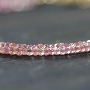 Op de afbeelding: Close-up van een delicate ketting met kleine, gefacetteerde roze edelstenen. De kralen zijn aan elkaar geregen, waardoor een subtiele curve ontstaat. De edelstenen hebben een zachte, doorschijnende uitstraling, wat een elegant effect geeft.