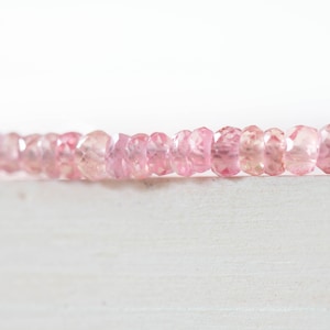 Op de afbeelding: Een streng gefacetteerde, lichtroze edelstenen. De kralen hebben een zachte roze kleur met variaties in tint, en zijn aan elkaar geregen. De achtergrond is helderwit, wat de delicate kleur van de kralen benadrukt.