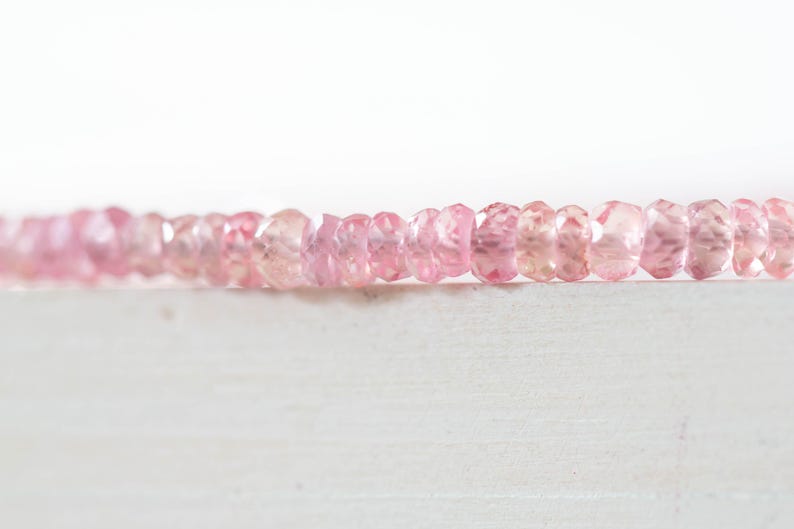 Op de afbeelding: Een streng gefacetteerde, lichtroze edelstenen. De kralen hebben een zachte roze kleur met variaties in tint, en zijn aan elkaar geregen. De achtergrond is helderwit, wat de delicate kleur van de kralen benadrukt.