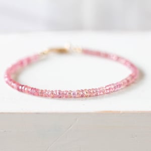 Op de afbeelding: Een delicate roze edelsteenarmband. De armband is samengesteld uit kleine, ronde, gefacetteerde roze edelstenen die aan elkaar zijn geregen. De sluiting is goudkleurig. De armband wordt gepresenteerd op een wit oppervlak.