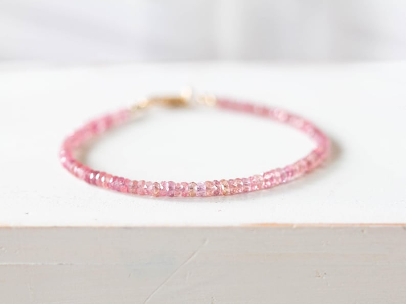 Op de afbeelding: Een delicate roze edelsteenarmband. De armband is samengesteld uit kleine, ronde, gefacetteerde roze edelstenen die aan elkaar zijn geregen. De sluiting is goudkleurig. De armband wordt gepresenteerd op een wit oppervlak.