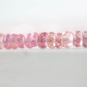 Op de afbeelding: Close-up van een streng gefacetteerde, roze edelstenen. De edelstenen hebben een zachte, lichtroze kleur, met variaties in tint. De kralen zijn aan elkaar geregen, waardoor een delicaat en elegant sieraad ontstaat.