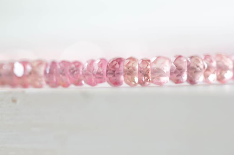 Op de afbeelding: Close-up van een streng gefacetteerde, roze edelstenen. De edelstenen hebben een zachte, lichtroze kleur, met variaties in tint. De kralen zijn aan elkaar geregen, waardoor een delicaat en elegant sieraad ontstaat.