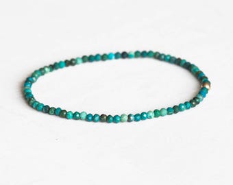 May include: A delicate bracelet featuring small, faceted turquoise beads. The beads are strung together, forming a circular shape. A small gold-colored bead is visible at the clasp. The bracelet is designed for everyday wear and adds a touch of color.