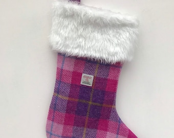 May include: Pink and purple tartan Christmas stocking with a white faux fur cuff. The stocking has a loop at the top for hanging.