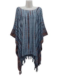 Op de afbeelding: Een blauw en bruin tie-dye poncho met een ronde hals en franje. Het lichte, vloeiende kledingstuk wordt op een mannequin gepresenteerd tegen een witte achtergrond. De poncho heeft een casual, bohemien stijl.