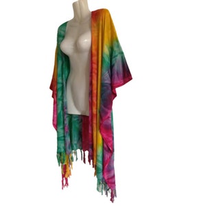 May include: A tie-dye kimono-style cover-up in a vibrant rainbow of colors, including green, yellow, orange, pink, and purple. The garment has long sleeves and fringed edges. It is displayed on a mannequin.