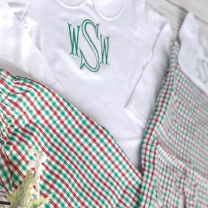 May include: White long-sleeved shirt and matching pants with a red and green plaid pattern. The shirt has a Peter Pan collar and a green embroidered monogram. The outfit is designed for children and is suitable for the holiday season.