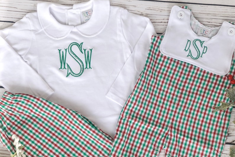 May include: White long-sleeved shirt and matching pants with a green monogram. The pants and romper feature a red and green plaid pattern. A white bib with a green monogram is also included.