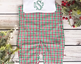 May include: A red, green, and white plaid baby romper with a white bib. The bib features a green embroidered monogram. The romper has snap closures and is made of a soft fabric. Festive holiday attire.