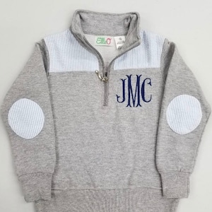 May include: Gray quarter-zip sweatshirt with blue and white striped accents on the shoulders and elbows. The sweatshirt has a navy blue monogram "JMC" on the chest.