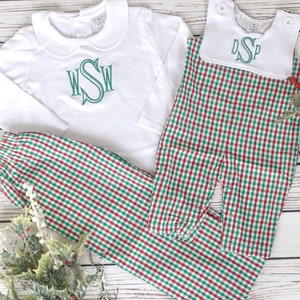 May include: White long-sleeved shirt and matching pants with a green monogram. The pants and a romper are red and green checkered. A white bib with a green monogram is also included. The clothing is designed for a baby or toddler.