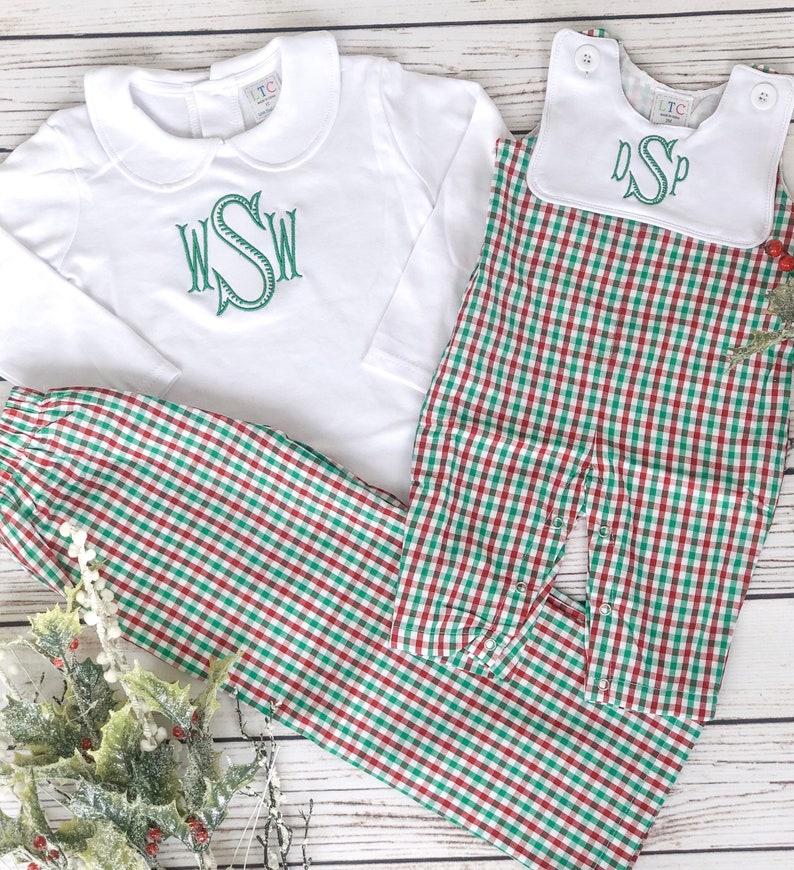 May include: White long-sleeved shirt and matching pants with a green monogram. The pants and a romper are red and green checkered. A white bib with a green monogram is also included. The clothing is designed for a baby or toddler.