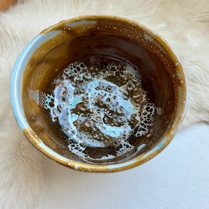 May include: A brown ceramic bowl with a light blue glaze and a speckled pattern. The bowl has a rounded shape and a slightly flared rim.