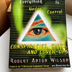 May include: A book cover with the title "Everything Is Under Control" featuring a pyramid with an eye. The book is by Robert Anton Wilson and discusses conspiracies, cults, and cover-ups. The cover has a green and black background.