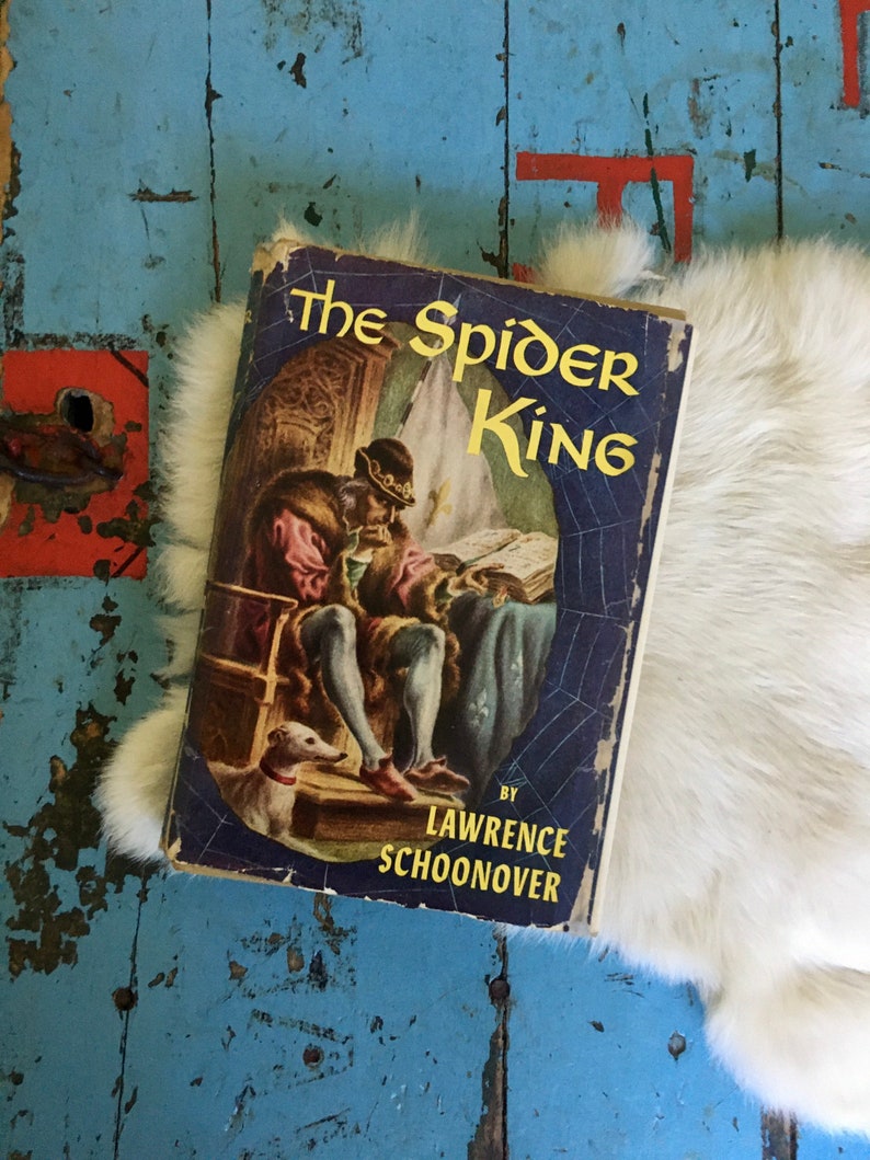 May include: A vintage paperback book titled "The Spider King" by Lawrence Schoonover. The cover features an illustration of a man in a crown and a dog, with a spider web design in the background.