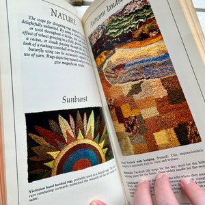 May include: A book open to a page with the title "Autumn Landscape" and a close-up of a hand-hooked rug depicting a landscape with hills, fields, and a sky. The text on the page describes the rug as "impressionistic" and mentions the materials used to create it, including tie-dyed silk strips, wool, and knitting yarns.