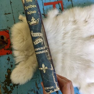 May include: A blue hardcover book titled "The Spider King" by Lawrence Schoonover. The book cover features a crown, a spider web, and the years 1423 and 1483.