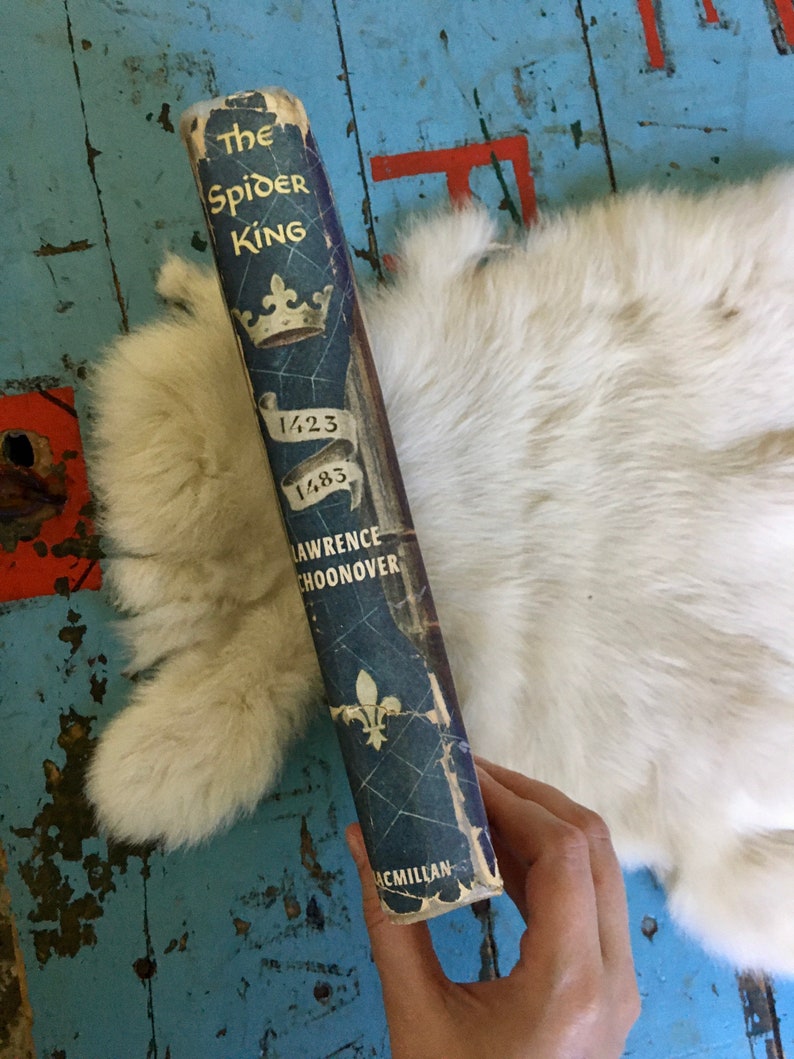 May include: A blue hardcover book titled "The Spider King" by Lawrence Schoonover. The book cover features a crown, a spider web, and the years 1423 and 1483.