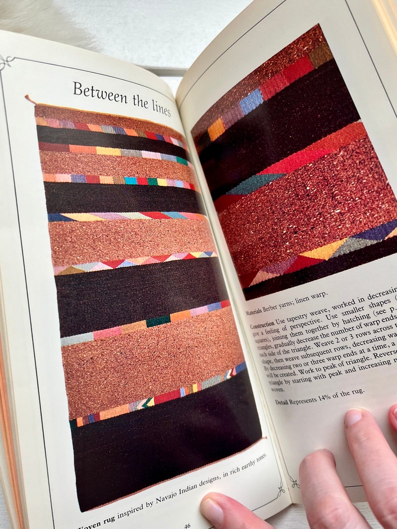May include: A book page with a colorful woven rug design and text that reads "Between the lines" and "Materials Berber yarns; linen warp." The text describes the construction of the rug, which is inspired by Navajo Indian designs.