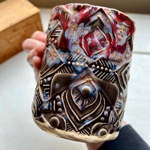 May include: A white ceramic mug with a black handle and the text "But First, Coffee" in a bold, black font. The mug is set against a blurred background, highlighting its clean design.