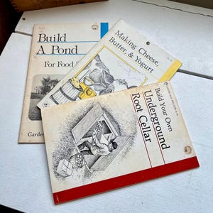 May include: Three vintage gardening books are stacked on a white surface. The titles include "Build A Pond", "Making Cheese, Butter, & Yogurt", and "Build Your Own Underground Root Cellar". The covers feature illustrations and text.