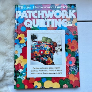 May include: A book titled "Patchwork & Quilting" by Better Homes and Gardens. The cover features a colorful patchwork quilt with a floral design. The text on the cover reads "Exciting quick-and-easy projects Quilting, Patchwork, Appliqué basics Heirloom and Contemporary designs."