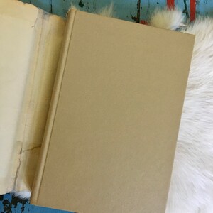 May include: A closed tan hardcover book with a white fur background.