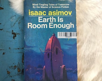 May include: A vintage paperback book cover featuring a futuristic illustration of a spaceship against a blue sky. The title of the book is "Earth Is Room Enough" by Isaac Asimov.